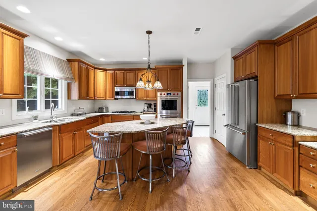 a kitchen with stainless steel appliances granite countertop a stove a refrigerator a sink dishwasher a dining table and chairs with wooden floor