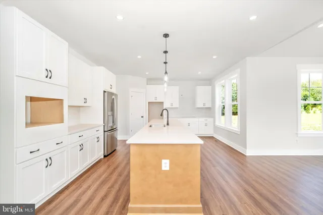 a large kitchen with stainless steel appliances a large counter top a sink a refrigerator and white cabinets