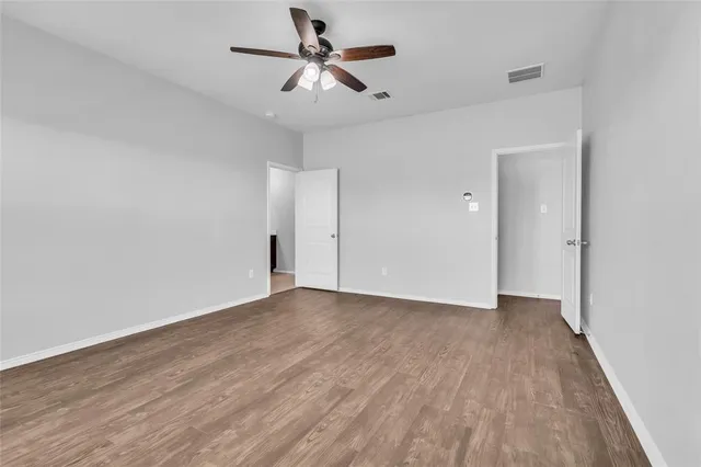 an empty room with wooden floor ceiling fan and window