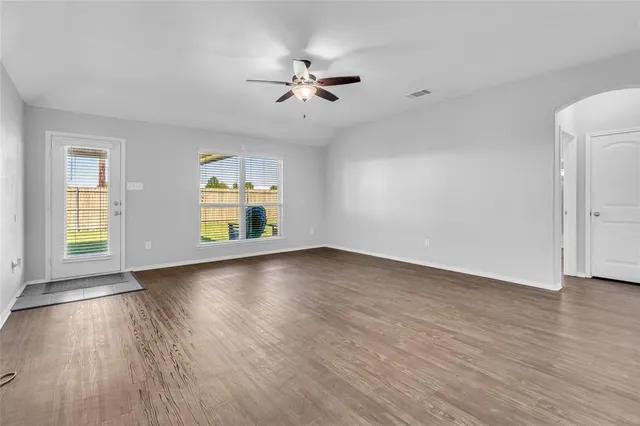 an empty room with wooden floor chandelier fan and windows