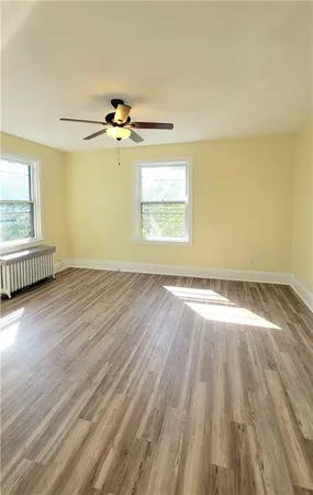 an empty room with wooden floor chandelier fan and windows