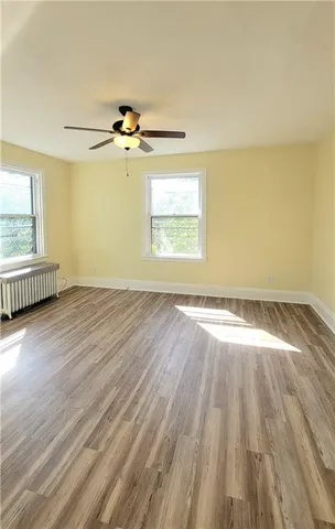 an empty room with wooden floor chandelier fan and windows