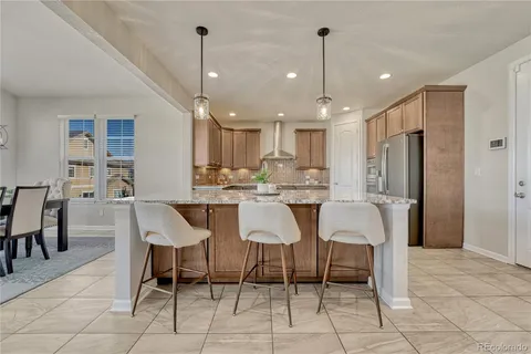 a kitchen with stainless steel appliances kitchen island granite countertop a dining table chairs and a refrigerator