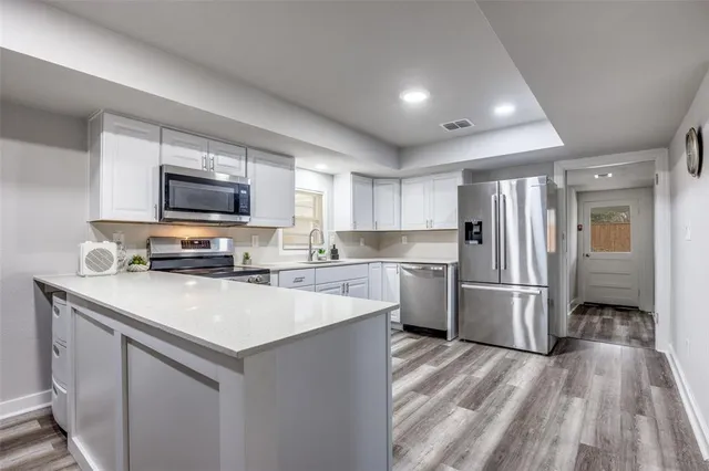 a kitchen with refrigerator a microwave a stove and white cabinets with wooden floor