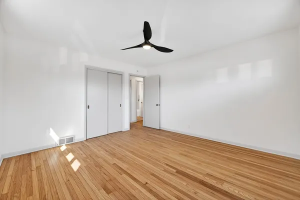 a view of empty room with wooden floor and fan