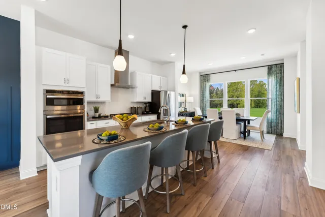 a kitchen with stainless steel appliances granite countertop a stove a refrigerator a kitchen island a dining table and chairs with wooden floor