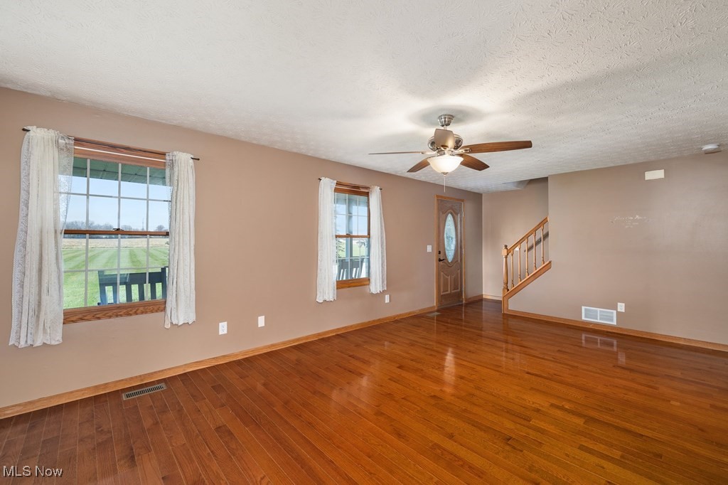 Empty room with hardwood / wood-style flooring, plenty of natural light, ceiling fan, and a textured ceiling
