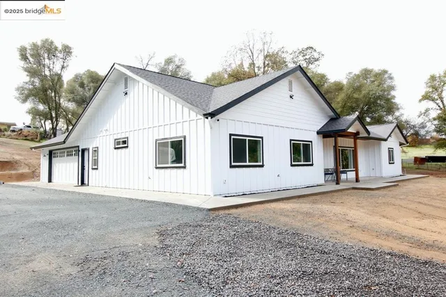 a view of a white house next to a yard with large trees