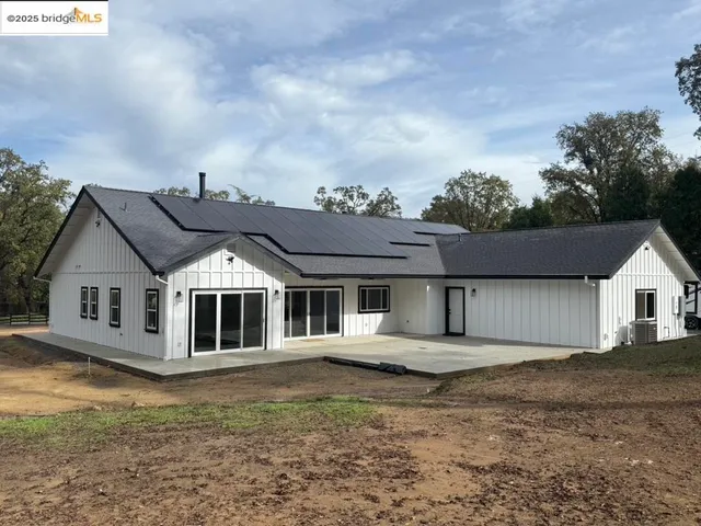 a view of a white house next to a yard with large trees