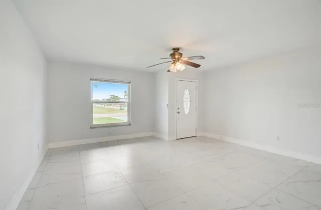 an empty room with a chandelier fan and windows