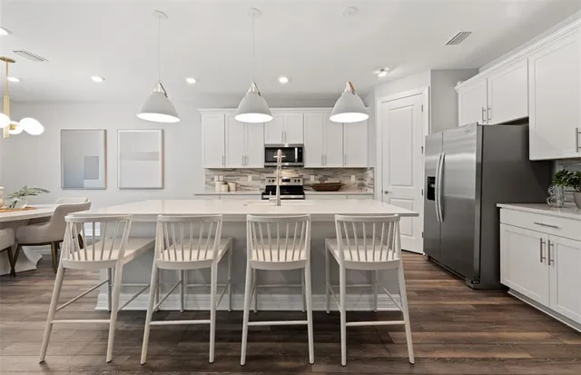 a kitchen with stainless steel appliances kitchen island granite countertop a dining table chairs refrigerator and microwave