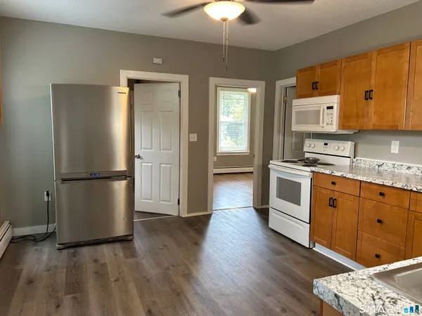 a kitchen with stainless steel appliances granite countertop a refrigerator a stove a sink and white cabinets with wooden floor