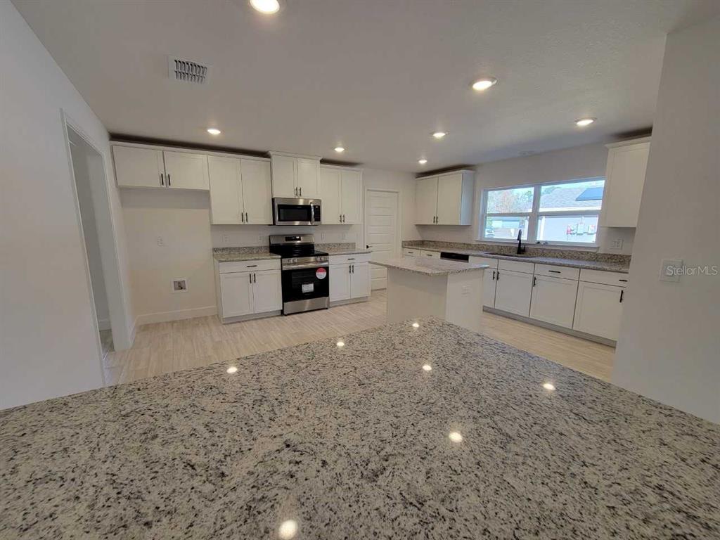 7035 Southwest 131st Loop Ocala, FL 34473 - Photo 5 of 28 a large kitchen with stainless steel appliances a large counter top a stove a sink a refrigerator and a sink