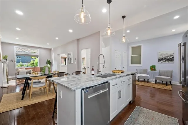 a kitchen with stainless steel appliances granite countertop a refrigerator a sink dishwasher a dining table and chairs with wooden floor