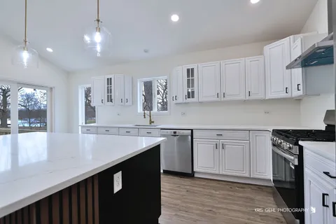a kitchen with stainless steel appliances granite countertop a sink dishwasher a stove and white cabinets with wooden floor