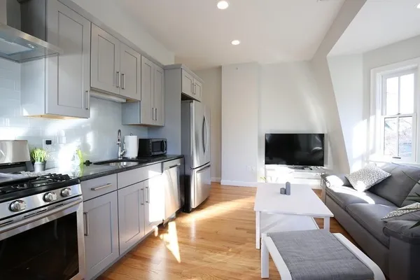 a kitchen with stainless steel appliances a stove a sink dishwasher a refrigerator white cabinets and wooden floor