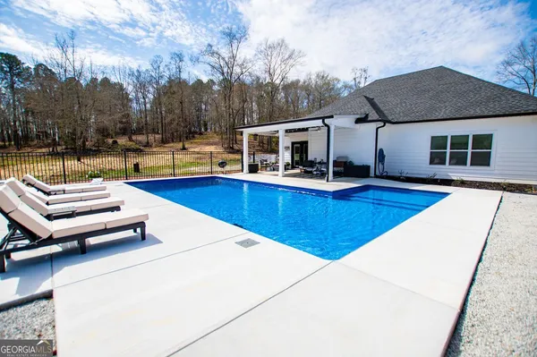 a view of a house with pool and chairs next to a yard
