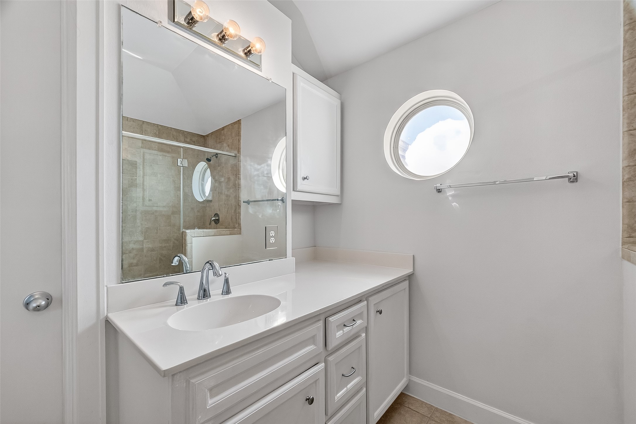 5951 S Loop East, Unit 47 Houston, TX 77033 - Photo 21 of 37 Primary bathroom features a clean, modern design with a large mirror, stylish vanity, and round window for natural light. The neutral tones create a bright and welcoming atmosphere.