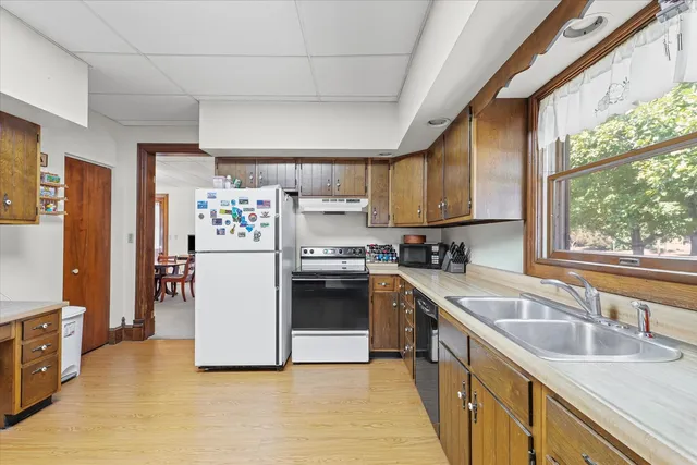 a kitchen with stainless steel appliances granite countertop a refrigerator a sink dishwasher a stove and a dining table with wooden floor