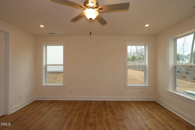 an empty room with wooden floor fan and windows