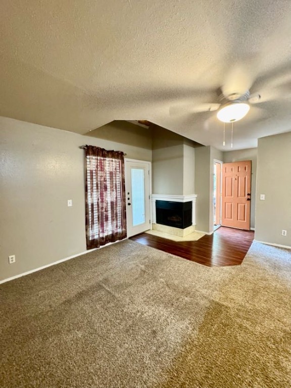 1305 West Villa Maria Road, Unit F105 Bryan, TX 77801 - Photo 7 of 26 Unfurnished living room featuring dark colored carpet, a textured ceiling, a multi sided fireplace, and a ceiling fan