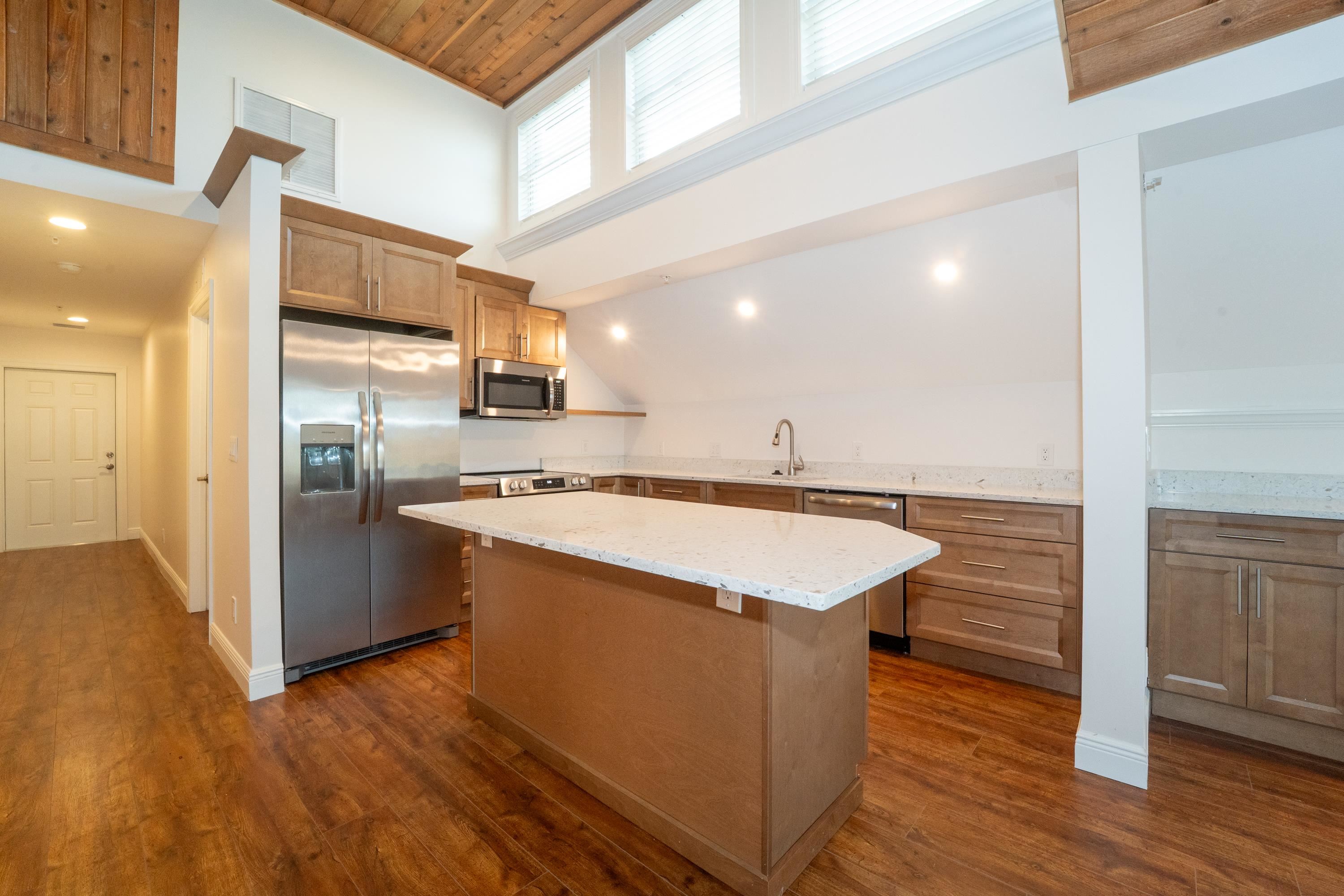11 Aviles Street, Unit 3C St. Augustine, FL 32084 - Photo 6 of 24 Kitchen featuring appliances with stainless steel finishes, light stone countertops, a center island, high vaulted ceiling, and dark wood finished floors