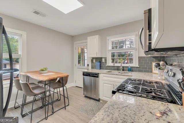 a kitchen with stainless steel appliances granite countertop a stove top oven a sink a dining table and chairs