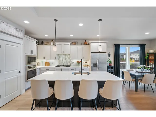 a kitchen with stainless steel appliances kitchen island granite countertop a dining table chairs and white cabinets