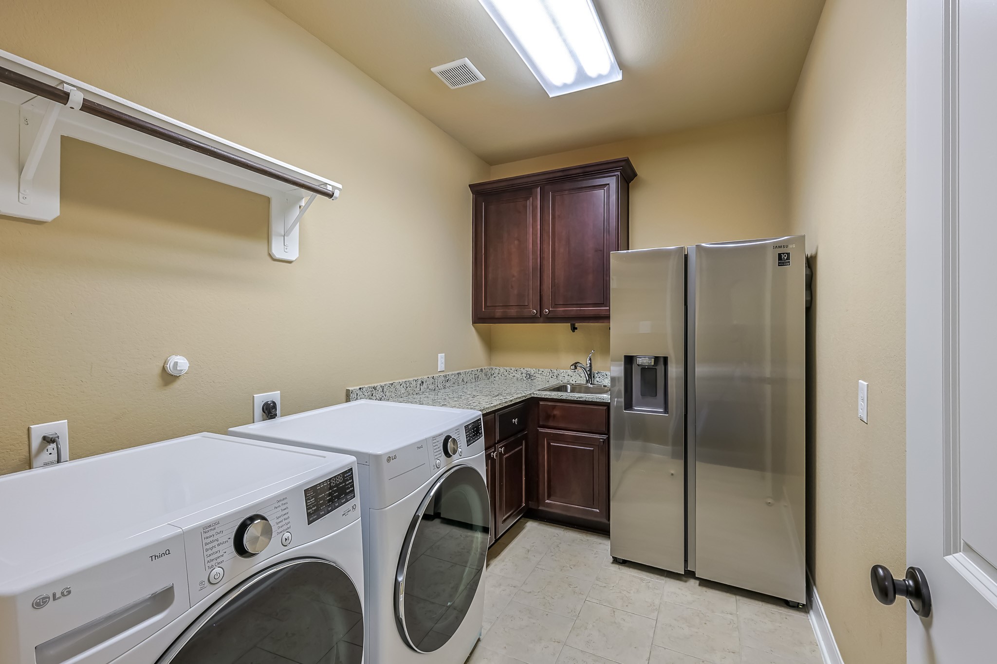 515 Mill Creek Road Pinehurst, TX 77362 - Photo 38 of 48 This laundry room features modern appliances, including a washer and dryer, ample storage with upper cabinets, a granite countertop, and a utility sink. The space is well-lit and includes a stainless steel refrigerator.