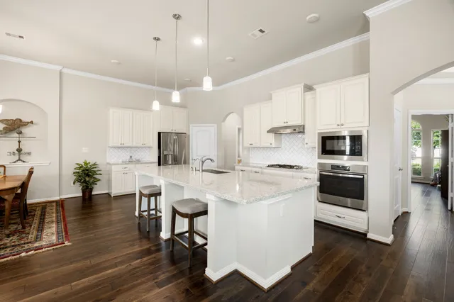 a kitchen with stainless steel appliances kitchen island granite countertop a stove a sink a refrigerator and a dining table with wooden floor