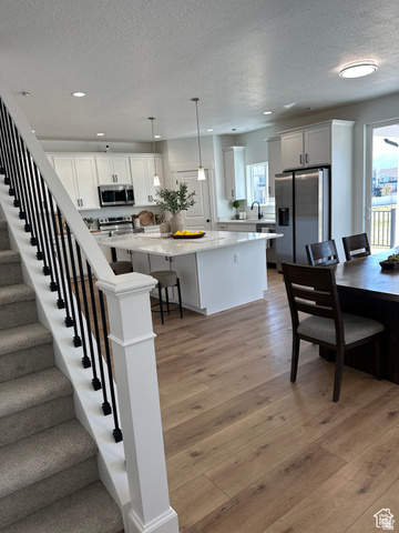 7927 Bristlecone Road, Unit 204 Eagle Mountain, UT 84005 - Photo 2 of 19 Kitchen with stainless steel appliances, light wood finished floors, a breakfast bar area, white cabinetry, and a textured ceiling