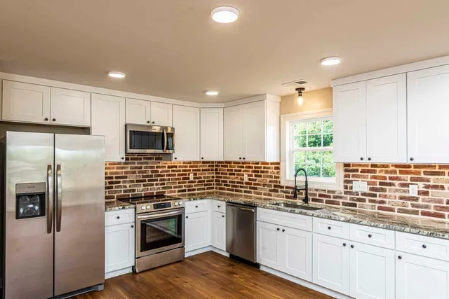 a kitchen with stainless steel appliances kitchen island granite countertop a sink a stove a refrigerator cabinets and a window