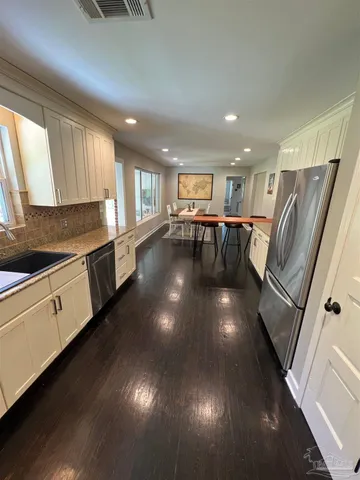 a kitchen with stainless steel appliances granite countertop a refrigerator a sink dishwasher a stove and a dining table with wooden floor