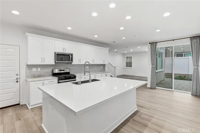 a large white kitchen with wooden floor a stove and a sink