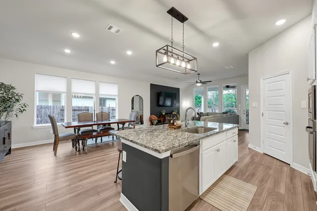 a kitchen with granite countertop a sink dishwasher a refrigerator and white cabinets with wooden floor