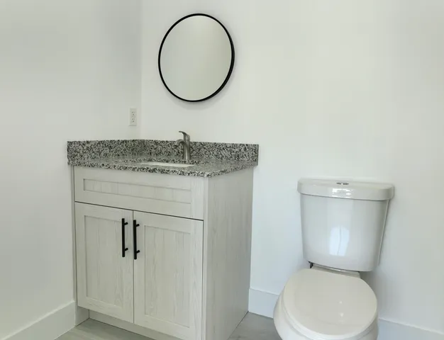 a bathroom with a granite countertop toilet a sink and a mirror