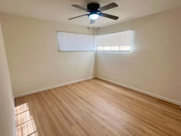 an empty room with wooden floor chandelier fan and windows