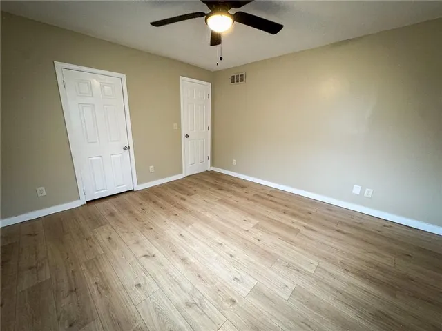 a view of an empty room with wooden floor and a ceiling fan