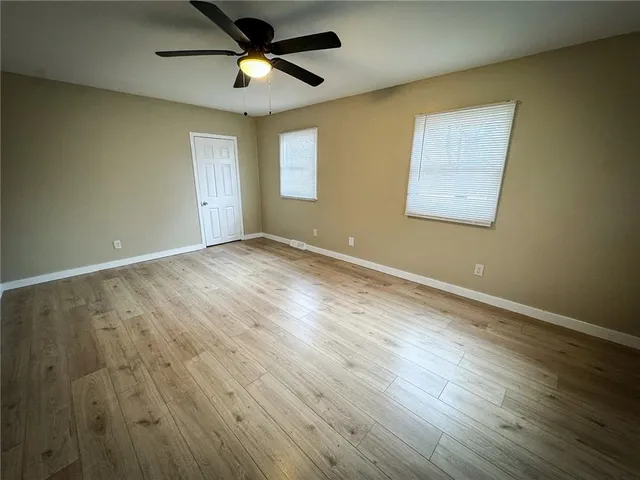 a view of an empty room with wooden floor and a ceiling fan