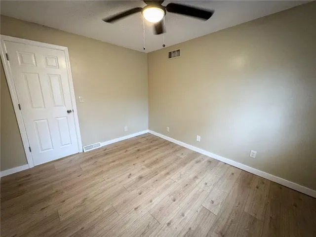an empty room with wooden floor fan and windows