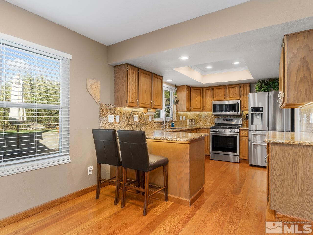 10060 Raintree Court Reno, NV 89511 - Photo 13 of 37 a kitchen with stainless steel appliances granite countertop a stove top oven a sink dishwasher and a refrigerator with wooden floor