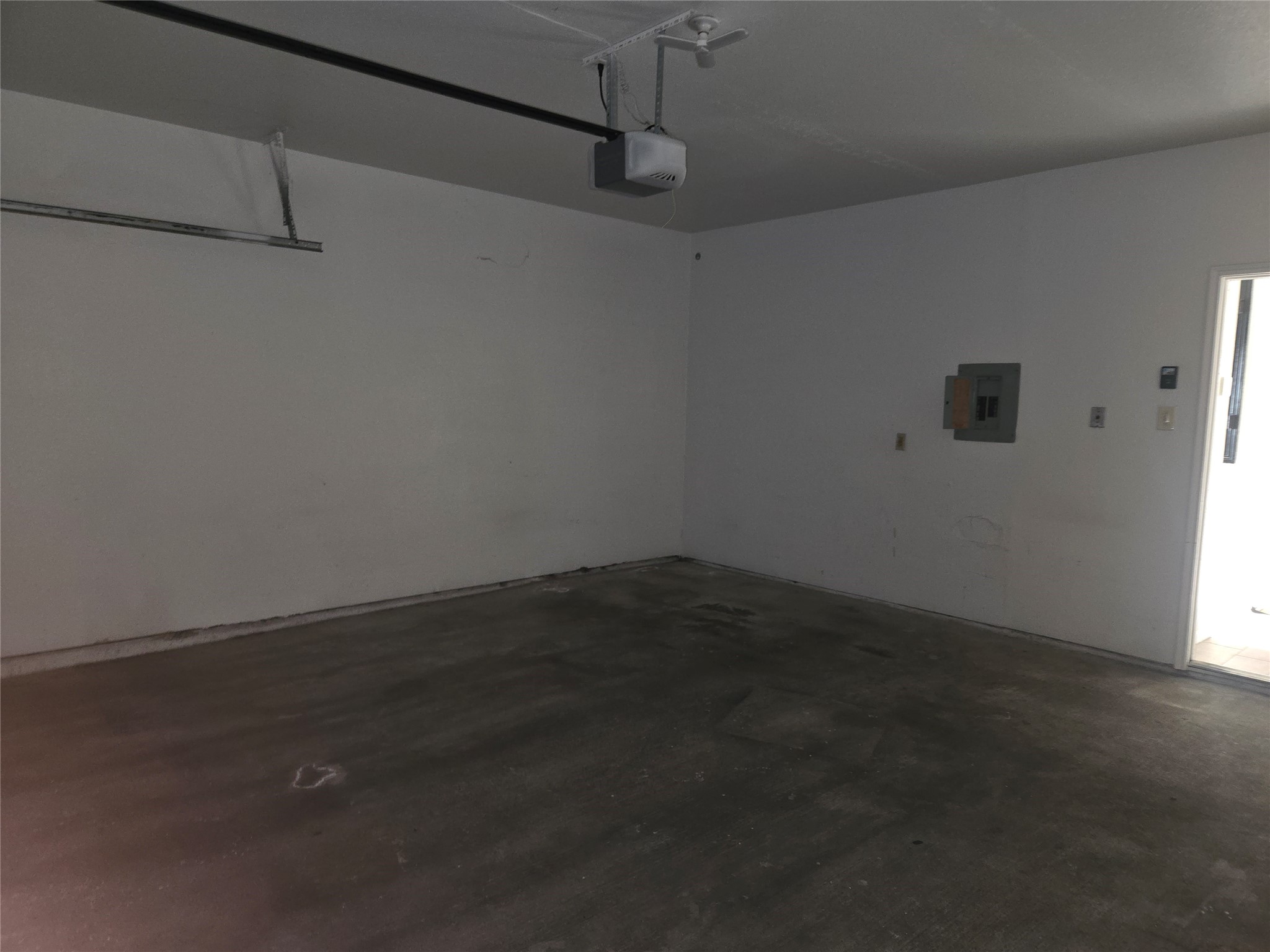 3780 Tanglewilde Street, Unit 501 Houston, TX 77063 - Photo 19 of 26 This photo shows a spacious garage with concrete flooring, white walls, a ceiling-mounted garage door opener, and an electrical panel. There's a door leading to the interior of the house.