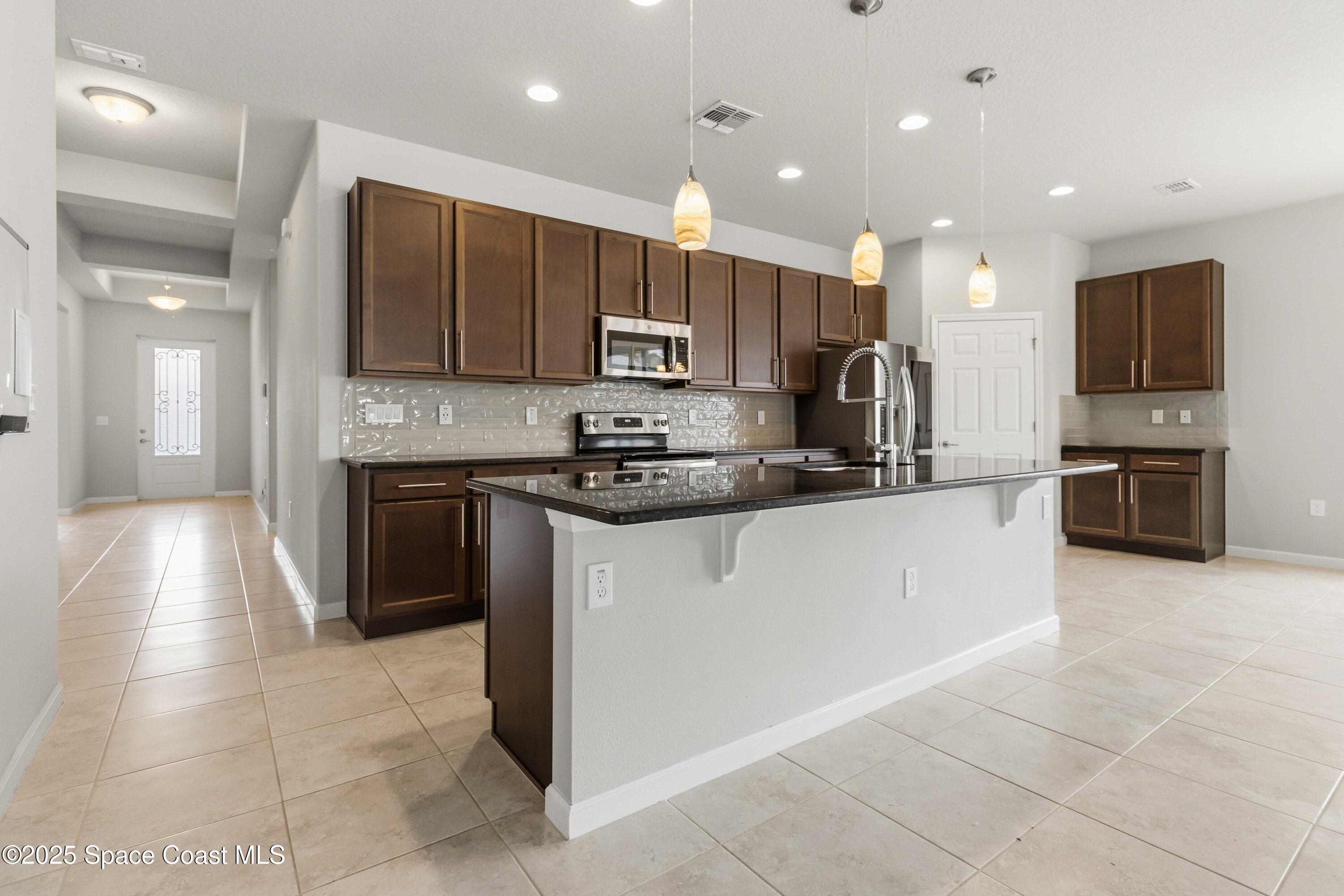 988 Corbin Circle Southwest Palm Bay, FL 32908 - Photo 3 of 26 a kitchen with kitchen island granite countertop a stove top oven a sink and a refrigerator