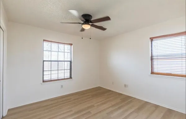 an empty room with wooden floor fan and windows