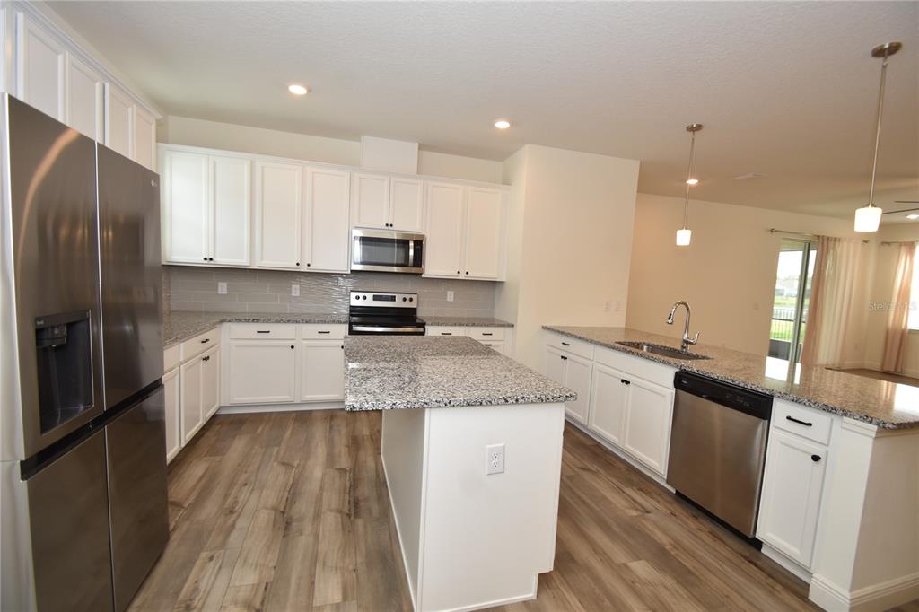 59 Oakleaf Way Palm Coast, FL 32137 - Photo 15 of 39 a large kitchen with stainless steel appliances granite countertop a stove a sink a refrigerator and white cabinets with wooden floor