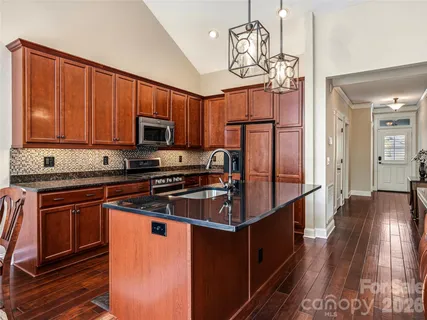 a kitchen with stainless steel appliances granite countertop a refrigerator a stove top oven a sink dishwasher and wooden cabinets with wooden floor