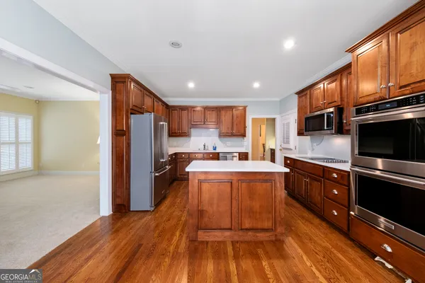 a kitchen with stainless steel appliances granite countertop a refrigerator a stove top oven a sink dishwasher and wooden cabinets with wooden floor