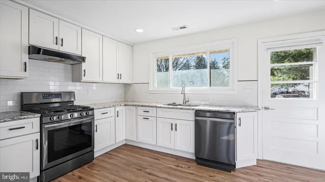 a kitchen with granite countertop a stove a sink and wooden floors