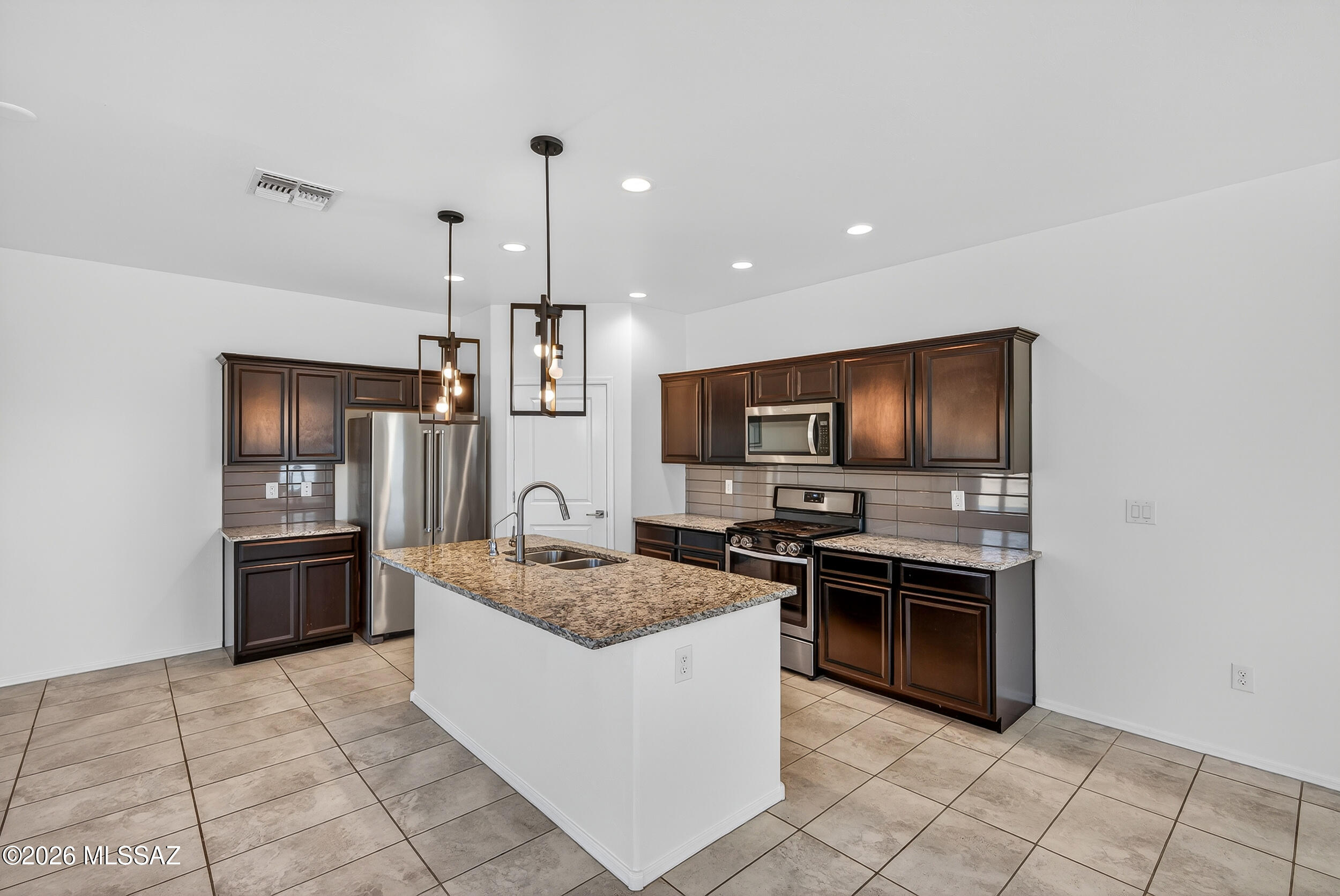 7556 South Circulo Rio Blanco Tucson, AZ 85756 - Photo 9 of 50 Stunning kitchen features a massive granite island with breakfast bar seating and elegant upgraded black-framed pendant lights.