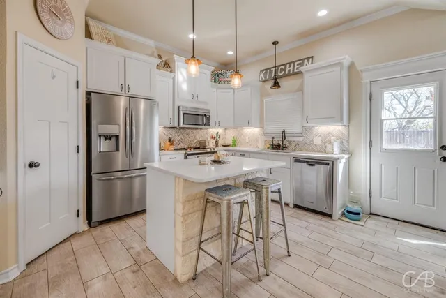 a kitchen with kitchen island a refrigerator a sink dishwasher a stove and white cabinets with wooden floor